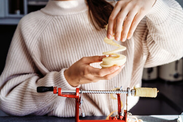 Close up of girl hands slicing and peeling apple using apple peeler corer slicer machine. Child cooking charlotte or apple pie