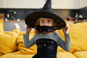 Funny child girl dressed in witch canival costume. Halloween holiday during quarantine time. Home patry