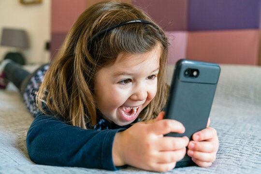 Joyful preschool girl using smartphone with pleasure while chilling at home