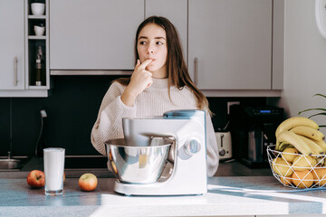 Teenager girl using mixer or food processor making dough.  Child cooking at modern kitchen, preparing apple pie tasting dough.