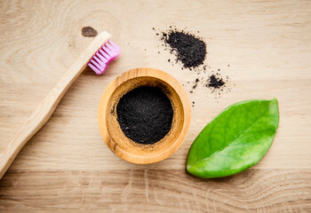 Raw activated charcoal powder in wooden cup and natural bamboo toothbrush next to it, green leaf for decoration. Charcoal toothpaste concept. Copy space.