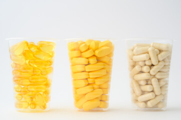 healthy diet nutrition concept of three plastic cups with pills softgels omega3 capsule vitamins tablets on white background with copy space