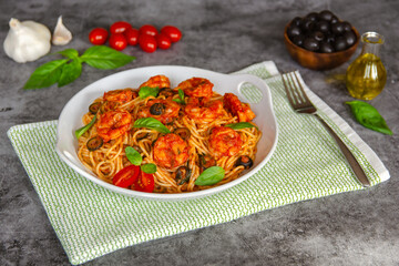 Pasta in tomato sauce with shrimps, olives, basil and garlic on a beautiful plate.