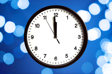 The white clock shows without five seconds midnight, on the bokeh background. Countdown to the new year.