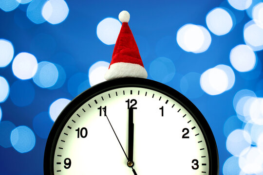 The white clock in red sunta hat shows without five seconds midnight, on the bokeh background. Countdown to the new year
