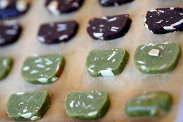 Uncooked/raw green tea and brown chocolate cookie dough arranged on baking sheet/paper. Close up view on white background.