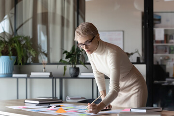 Fototapeta na wymiar Focused young Caucasian businesswoman in glasses consider work with paper company financial project in office. Serious 30s female employee brainstorm analyze paperwork documentation at workplace.