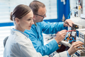 Two electronic engineers on the test bench measuring a new product © Kzenon
