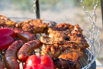 Chicken, sausages and red bell pepper being barbequed