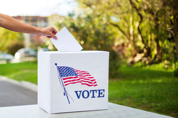 Hand putting vote into ballot box on table outside.