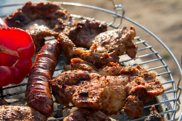 Chicken, sausages and red bell pepper being barbequed