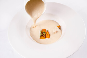 Sunroot cream soup served with some pumpkin and pine nuts being poured into a plate