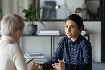 Multiracial female colleagues talk discuss company financial business project in office. Concentrated diverse multiethnic women coworkers or partners speak brainstorm at meeting or briefing together.