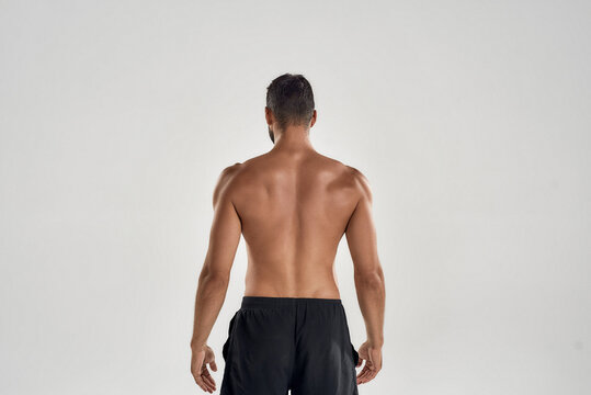 Rear view of muscular man with naked posing isolated over grey background, studio shot