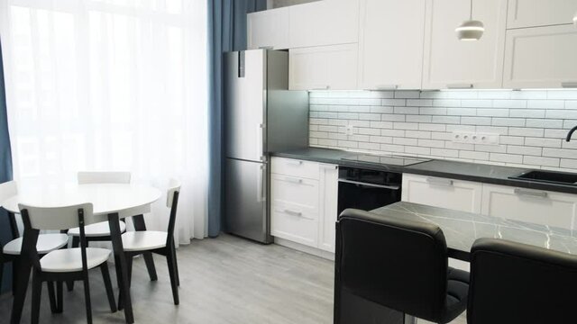 Steadycam shows elegant modern kitchen with white walls. Light interior of a white kitchen in a compact apartment, black and white furniture. Ceramic tiles on the wall and wooden countertop 4k