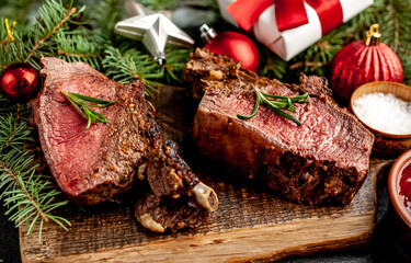  Christmas Dinner for Two. Baked Beef on the Bone with Spices on a Stone Table with a Christmas Tree and New Year's Toys