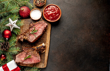 Christmas Dinner for Two. Baked Beef on the Bone with Spices on a Stone Table with a Christmas Tree and New Year's Toys  with copy space

