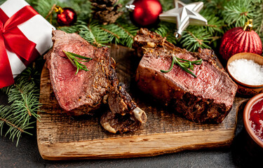 Christmas Dinner for Two. Baked Beef on the Bone with Spices on a Stone Table with a Christmas Tree and New Year's Toys