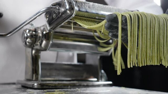 Traditional Italian cuisine. making pasta on machine for cutting pasta. Slow motion. Dough slicing machine. pasta making machine to make fresh spinage tagliatelle. Full hd