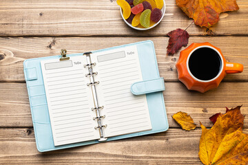 Top view composition with pumpkin styled cup of coffee and autumn themed decoration, fallen leaves and notebook on wooden background. Flat lay, copy space