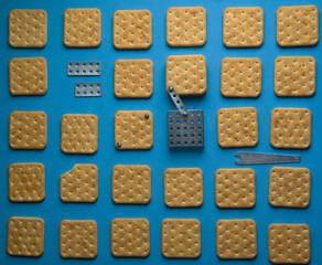 Crackers and constructor details on a blue background. Nuts and screws. Synesthesia. Iron cookie. An edible puzzle. High quality photo. Conceptual still life. Product photography. Different objects