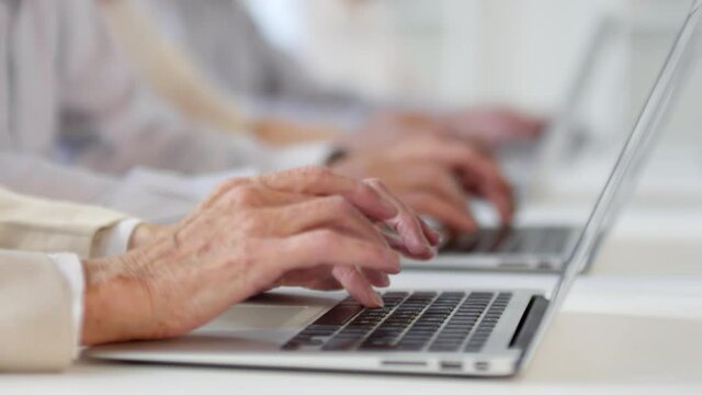 Sequence of shots of cheerful senior men and women with grey hair sitting at desks and using laptops in computer class as male middle-aged teacher with beard monitoring their progress and helping
