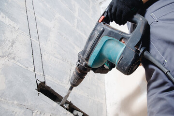 Builder worker man using jackhammer to drill into construction wall for duct for air conditioning...