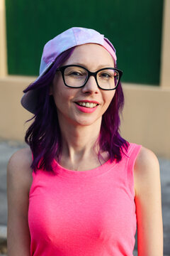 Young casually dressed Caucasian woman wearing pink, smiling while looking at the camera with confidence and interest in the warm evening light