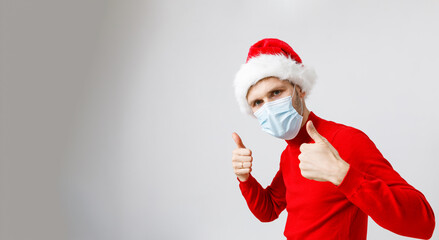 Fototapeta na wymiar Beautiful man wearing disposable protective face mask and Santa hat. Male model wearing red sweater on white isolated. Christmas concept during pandemic of COVID-19 Coronavirus respiratory viruses 