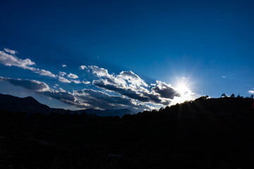 sunrise beams rising over a mountain cliff  with blue sky and low puffy clouds near Colorado Springs, Colorado, USA.