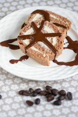 Coffee Swiss roll two slices drizzled with dark chocolate on glass decorated white plate, spilled fresh coffee beans