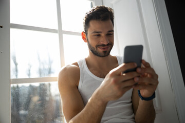 Cropped shot of man sitting on windowsill with mobile phone