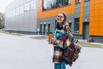 female college student holding notebooks smiling standing in university campus. happy woman in braces and glasses education learning high school program. smart teen nerd with backpack walking outdoor