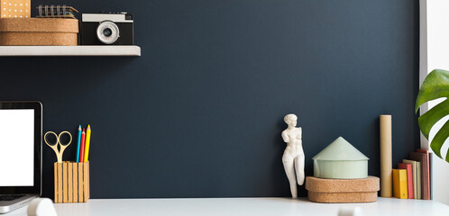 Desk, vintage style workspace and dark blue wall background with camera, books and figurine. Mockup.