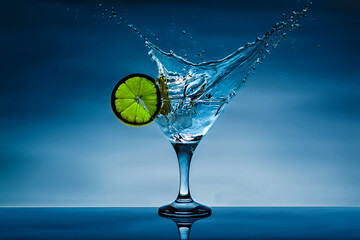 Alcohol cocktail with splash and green lime isolated on blue background. Vermouth cocktail inside...