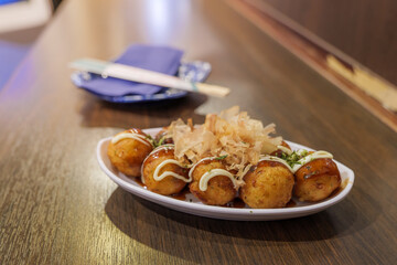 Selective focus at Takoyaki or Japanese octopus balls, serve on white plate on wooden counter in Japanese restaurant.
