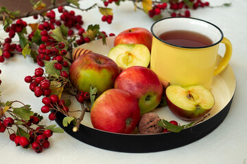 Cozy autumn hot spiced tea with honey, apples and red hawthorn berries on a tray. Still life on white background