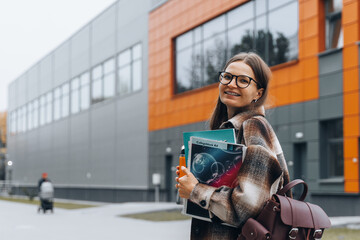 Portrait of girl student standing at university campus. Laughing Woman wearing braces, eyeglasses, bag with books having coffee break after lecture. Enjoying College life. Learning education concept.