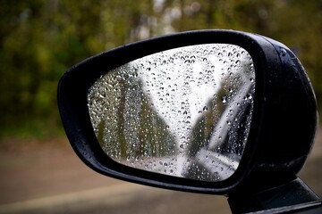 sideview, rearview mirror of a car on road with drops of rain at autumn rainy day '