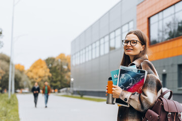 college female student with book, coffee smiling walking on university campus. happy woman in braces glasses. education learning high school concept. smart teen nerd with backpack enjoying autumn