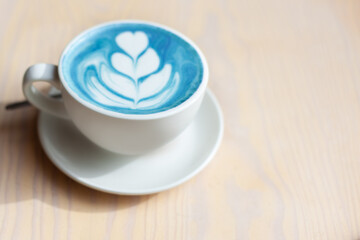 cup of hot butterfly pea latte or blue spirulina latte on wooden table