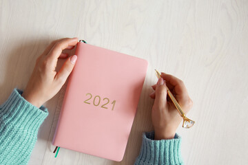 Woman sitting in knitted warm sweater with coral coloured 2021 diary on table