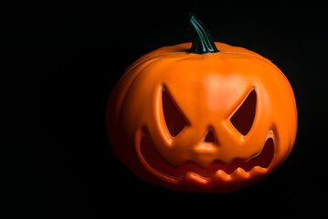 Ghostly isolated plastic Halloween orange pumpkin with scary face on black background with copy space