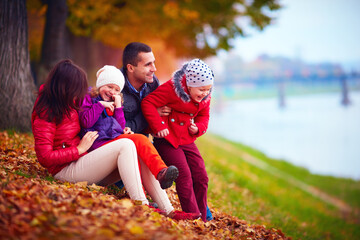 smiling family having fun among fallen leaves in autumn park