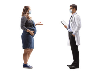 Full length profile shot of a doctor and a pregnant woman talking with protective face masks