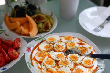 Boiled eggs with yoghurt sauce, tomato salda and various fruit on the breakfast table. Selective focus.