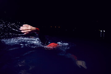 Obraz na płótnie Canvas triathlon athlete swimming in dark night wearing wetsuit
