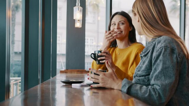 Female friends enjoying talking in a coffee shop. Two women sitting at cafe table drinking coffee and chatting. 
