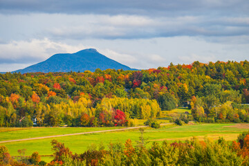 view of rural farm fields and forests  with Camels Hump Mountain in fall foliage season, in Vermont
