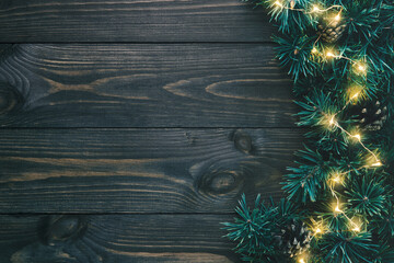 Fir branches and christmas lights on dark wooden background with copy space. Flat lay, top view.